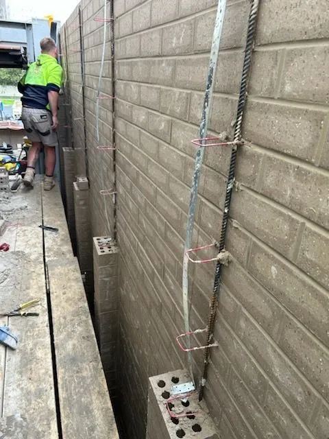 Masonry worker beside a grey blockwork boundary wall under construction