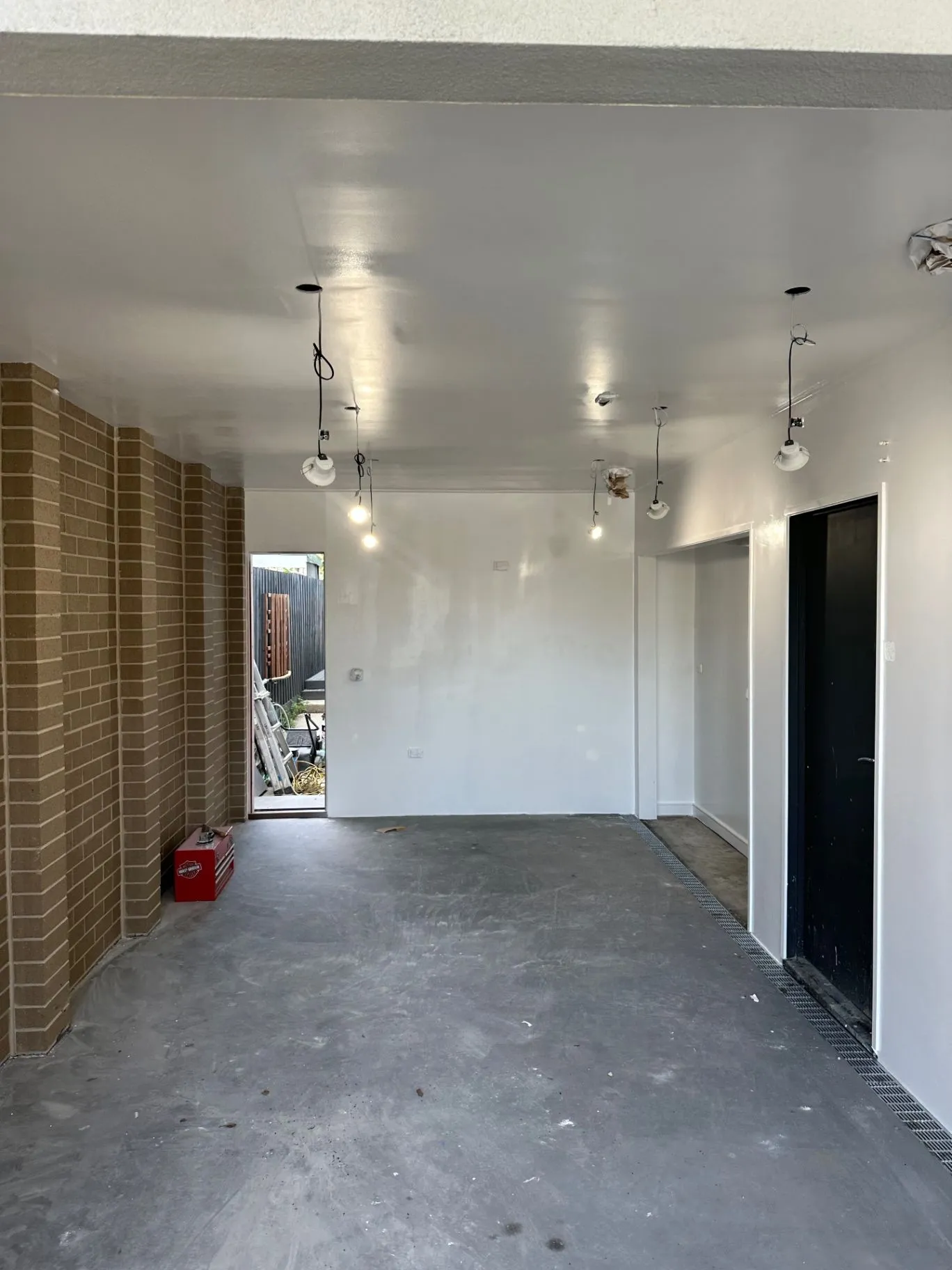 Covered interior workspace with white ceiling, black doors, exposed brickwork, and hanging lights
