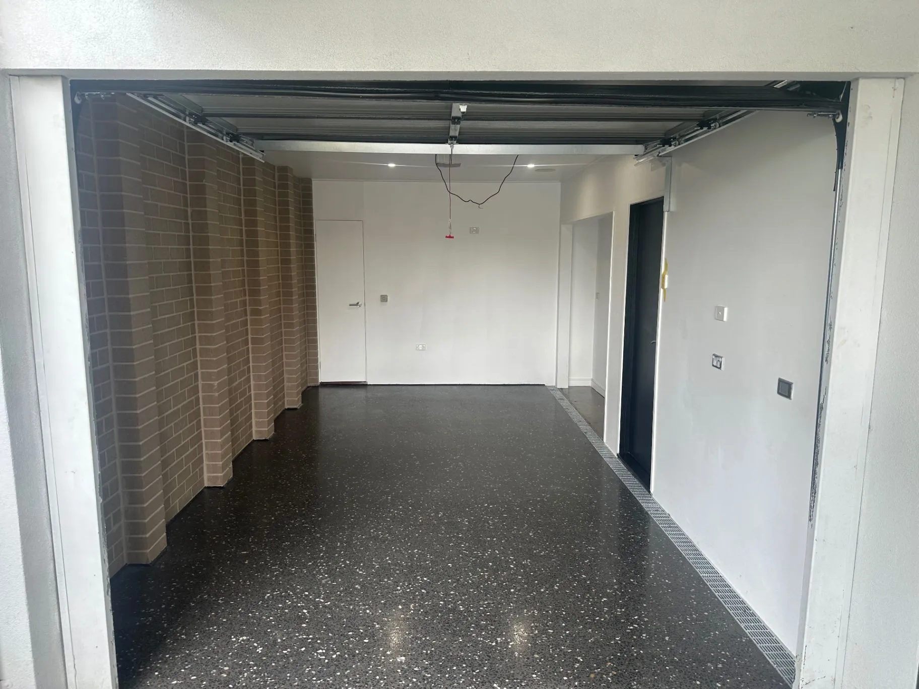 Finished interior workspace with a dark speckled floor, exposed brickwork, and open garage door