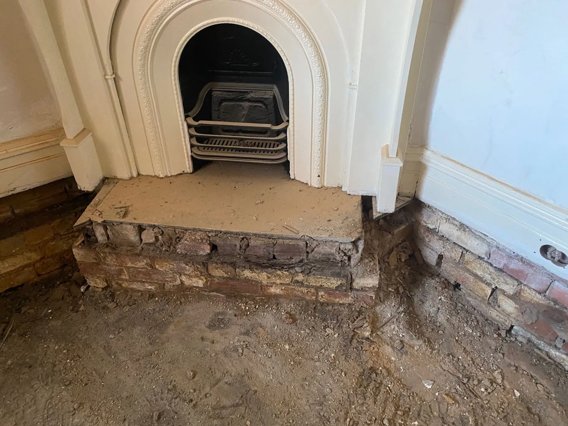 Ornate fireplace surround with hearth and exposed brickwork during repair work