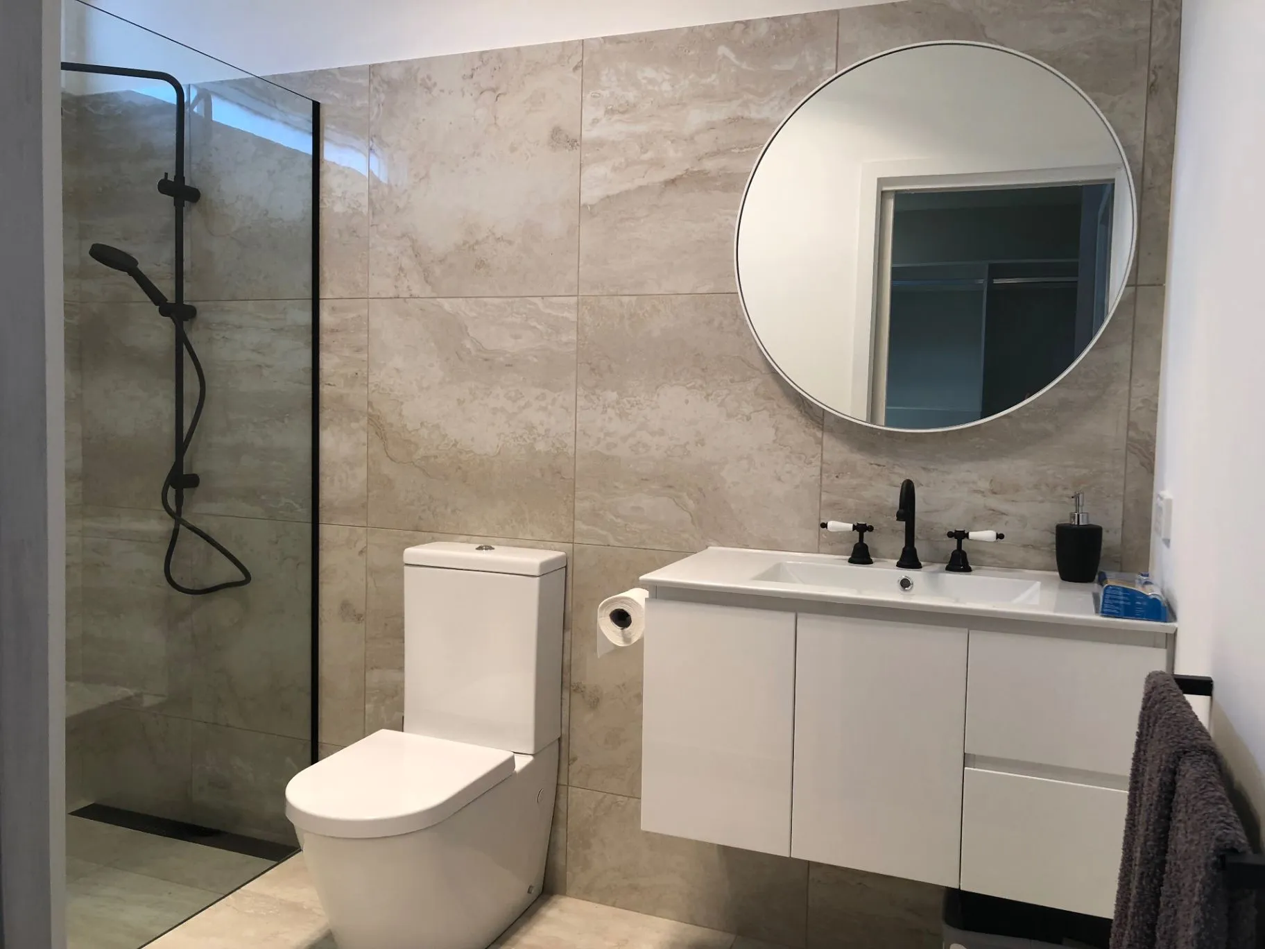 Finished Kyneton bathroom with stone-look wall tiles, shower, vanity, and round mirror
